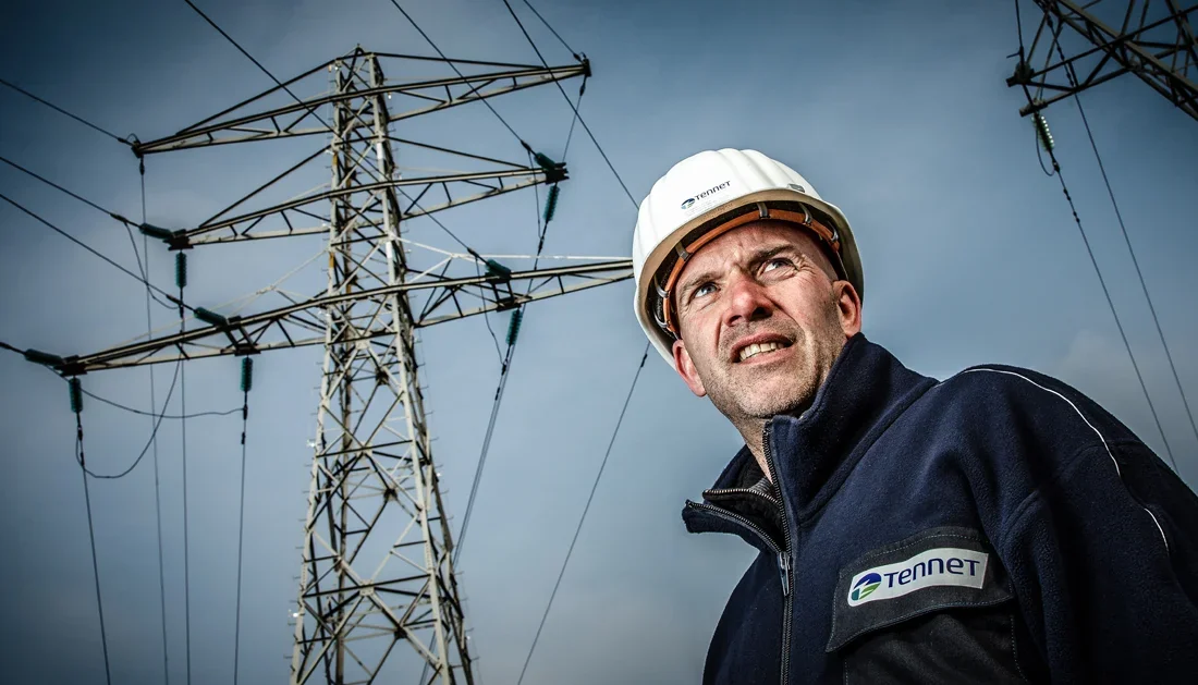 Ingenieur met helm onder een hoogspanningsmast