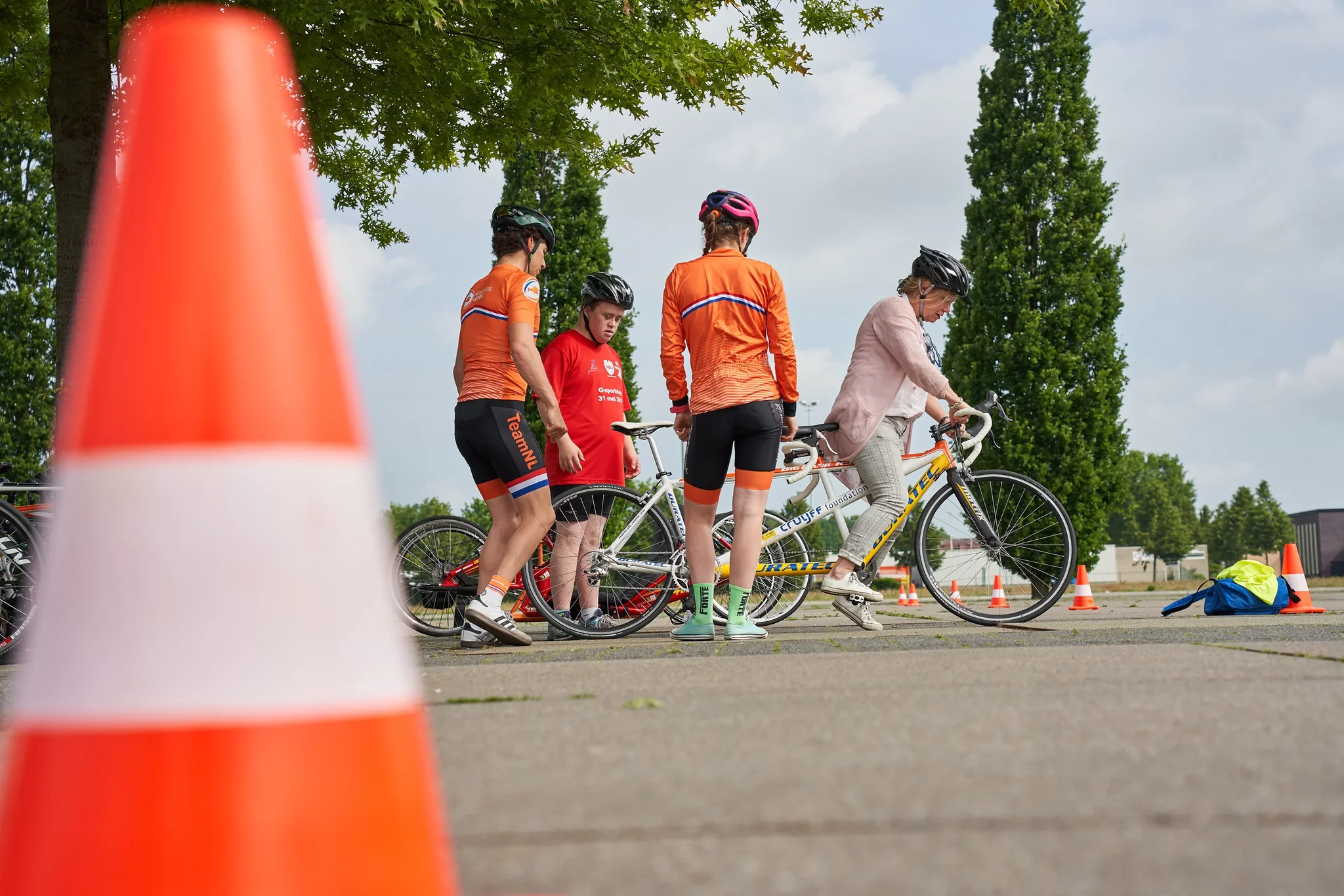 Groep fietsers in oranje tenues met een tandemfiets