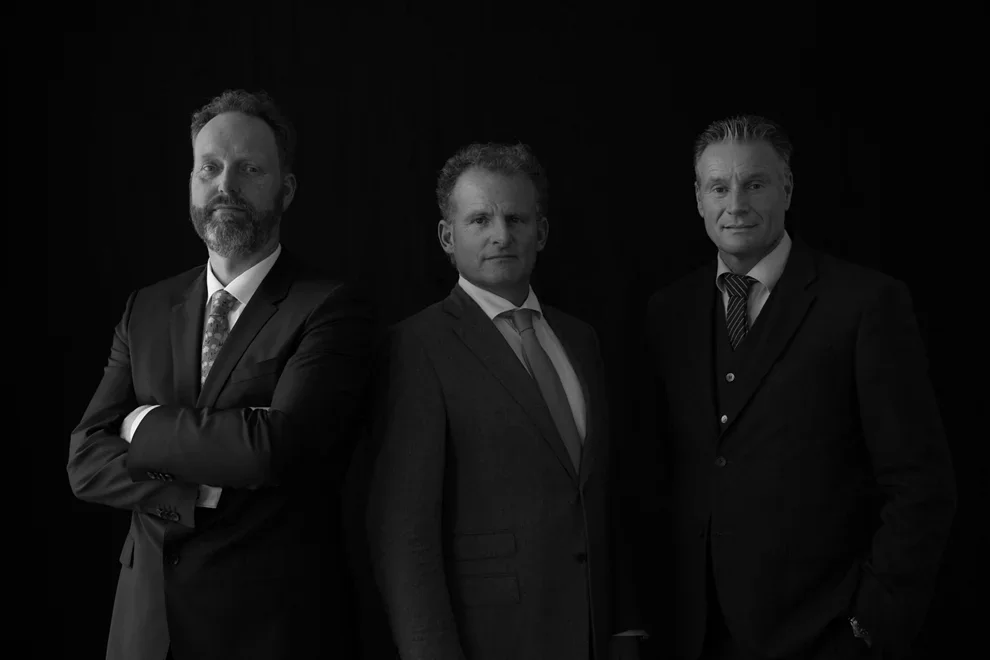 Formeel zwart-wit groepsportret van drie mannen in donkere pakken