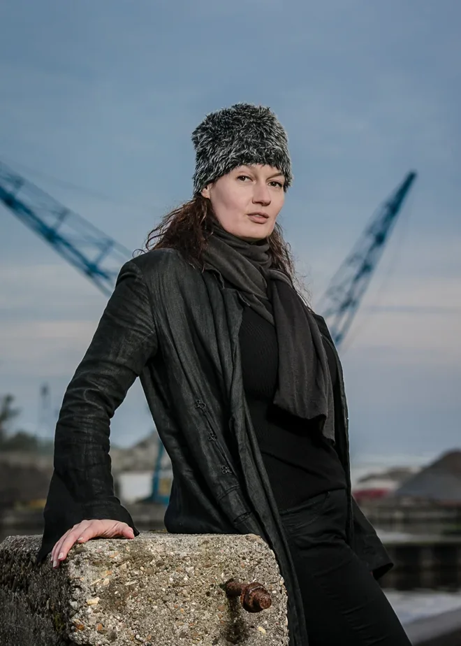 Vrouw in donkere jas met industriële havenkranen op de achtergrond