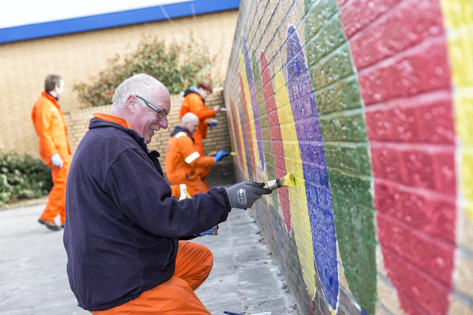 Vrijwilliger in oranje pak schildert een kleurrijke muurschildering