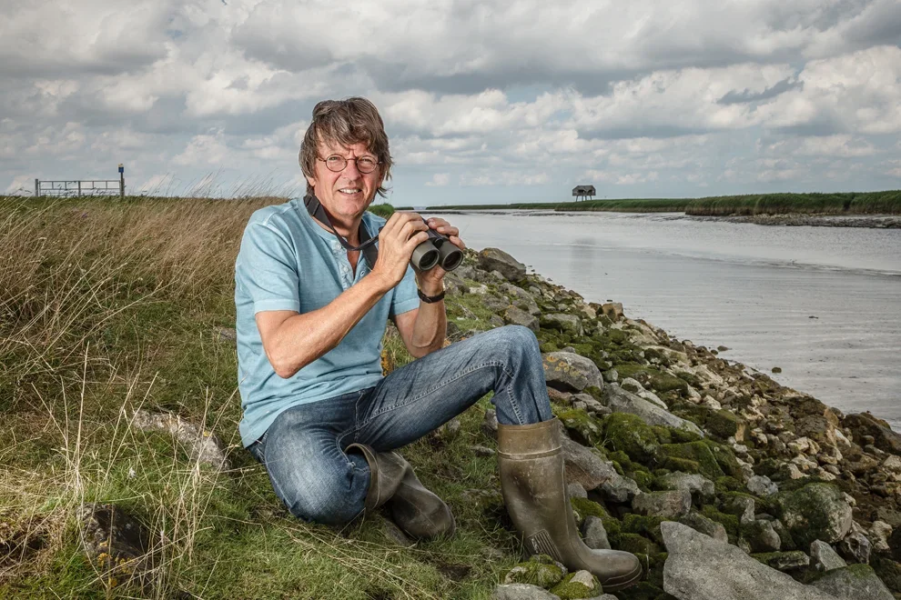 Man zit op rotsen bij het water met een verrekijker